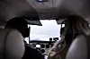 Interiør i et lite fly med to personer foran, instrumenter og utsikt mot himmel og terreng gjennom frontruten.