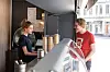 To personer snakker ved disken i en kafé med kaffekopper og vindu ut mot gaten.