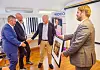 Fire menn snakker sammen i et kontorrom med bilder, stativ og et MDCO-skilt i bakgrunnen.