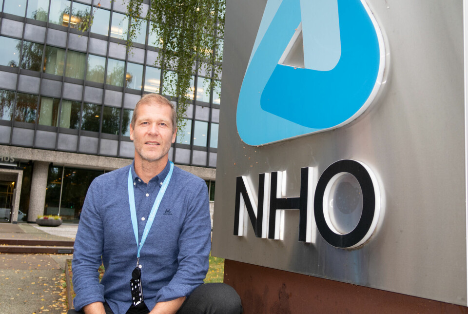 Arne Stadheim på huk utendørs foran et skilt med NHO-logo