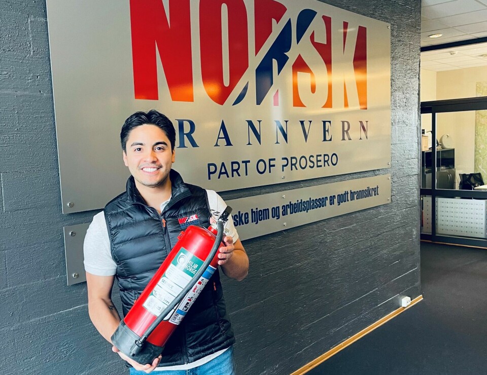 Daniel Morales står og holder i et brannslukkungsapparat foran et skilt med logoen til Norsk Brannvern